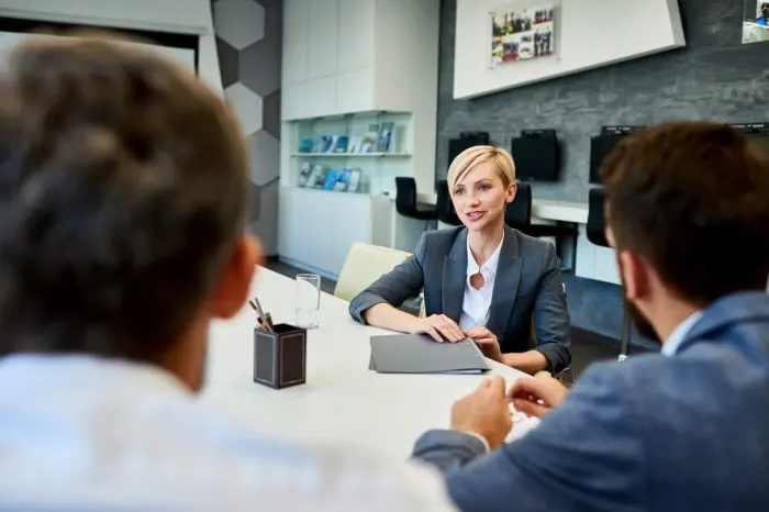 smiling businesswoman talking to partners 68Y9JC9 e1650789216898